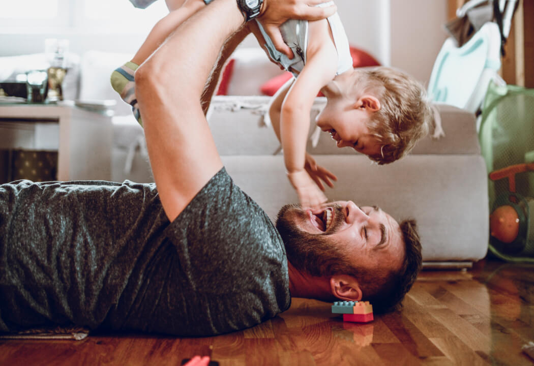 Dad playing and holding up a toddler in a living room