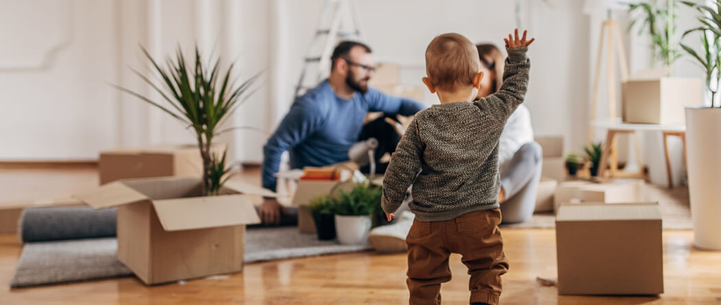 toddler walking through a room full of moving boxes toward parents in the background