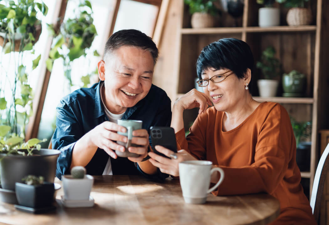 Older couple sitting at a table with coffee cups and looking at a smartphone